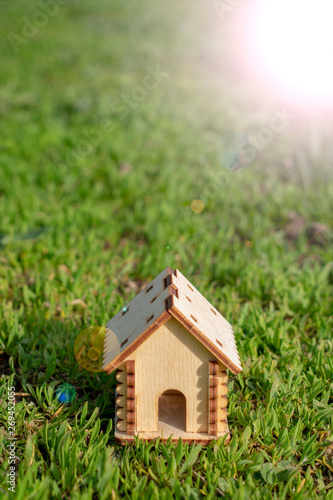 Toy wooden house on the bright grass. Sun glare on the right side. Copy space. Real estate concept, business loan financing concept, new house concept.