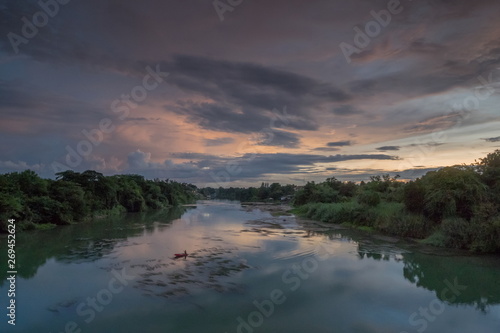 Fototapeta Naklejka Na Ścianę i Meble -  river view evening of a fishing boat floating in Mae Klong river around with forest on both bank with cloudy sky background, Ban Pong District, Ratchaburi, Thailand.