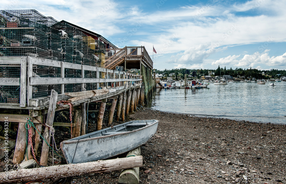 Fototapeta premium New England Fishing Port: A small boat waits beside a rough wooden pier piled high with lobster traps on a bay in southeast Maine.
