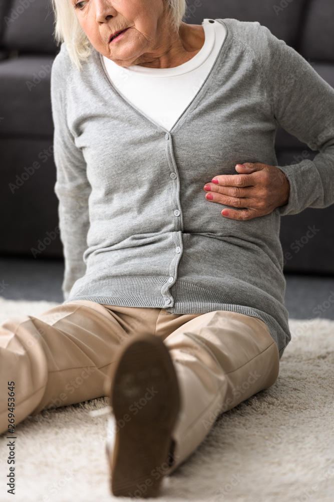 partial view of senior woman with heart attack sitting on carpet partial view of senior woman with heart attack sitting on carpet