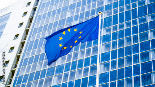 Image of EU flag fluttering on wind against high business office building made of concerete and glass. Concept of ecenomics, development, government and politics photo