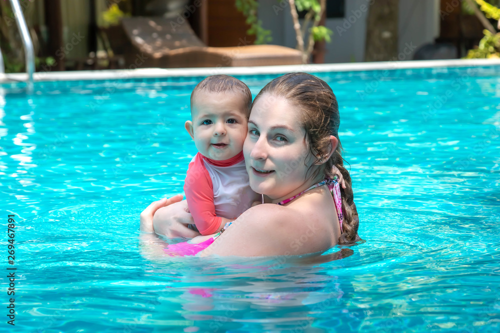 Happy mother with little baby daughter swims in the pool at summer holiday. Sunny day. Tropics. Infant watching to camera