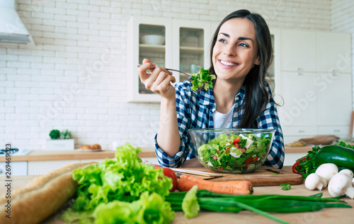 Healthy lifestyle. Good life. Organic food. Vegetables. Close up portrait of happy cute beautiful young woman while she try tasty vegan salad in the kitchen at home. photo