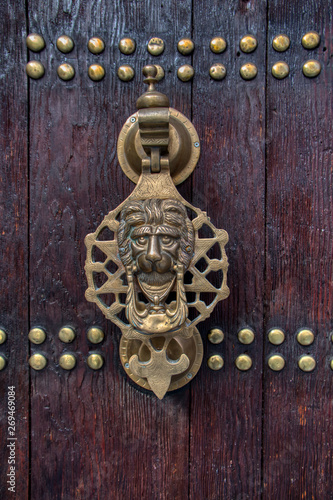 Detail of the bronze knocker of an old wooden door decorated with nails. This Arabic style door is located in the city of Chaouen, Morocco. photo