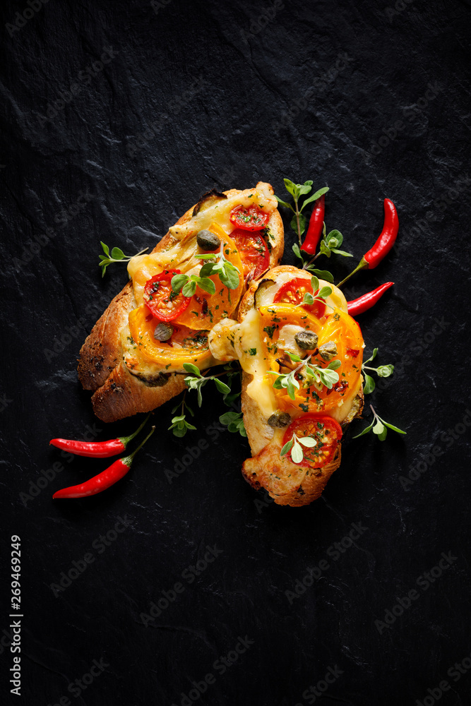 Bruschetta, grilled baguette with addition of  tomatoes, cheese and herbs on a black background, top view. Vegetarian appetizer. 