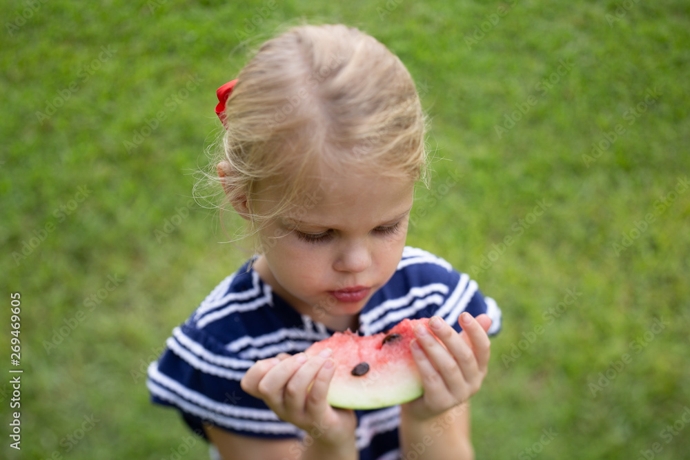 Blonde haired blue eyed 4 year old girl eating watermelon in summer