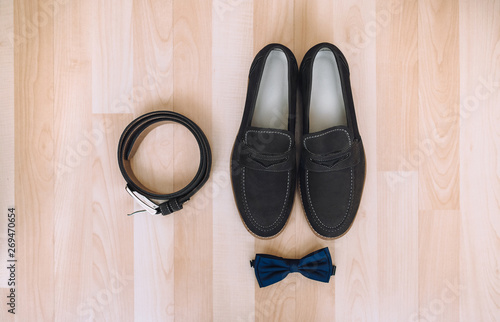 Wedding details, morning groom. Leather shoes, bow tie and belt lie on the background of beige parquet. Composition and concept.