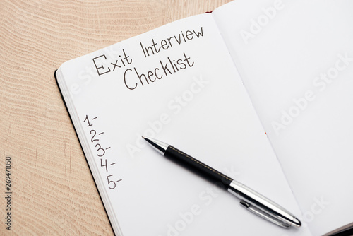 notebook with pen, exit interview checklist lettering and numbers on wooden table