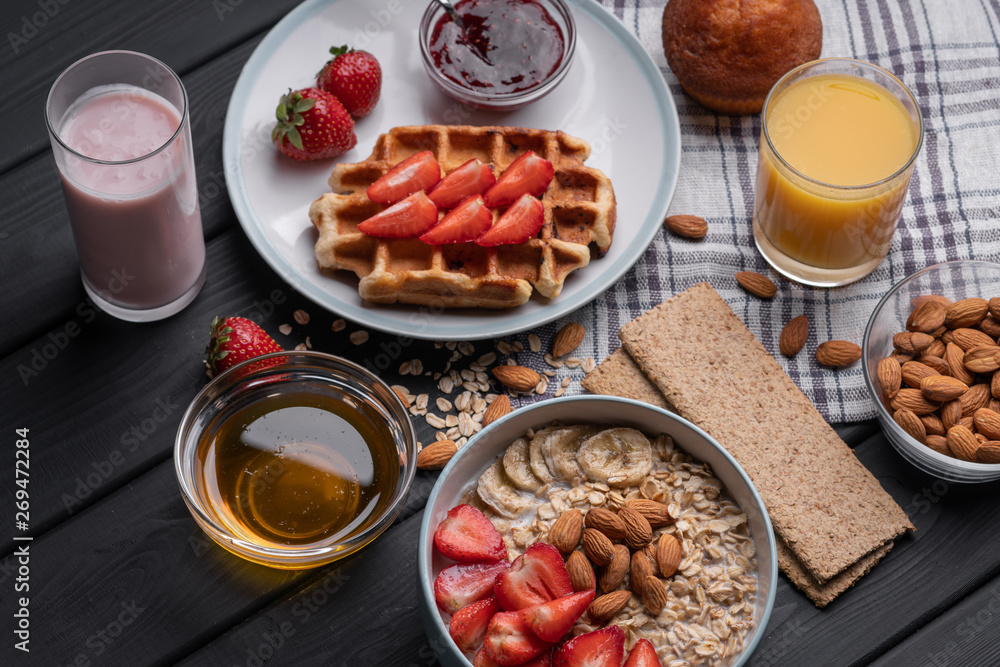 Morning meal set. Breakfast. Delicious oatmeal granola with berries, nuts and honey. A crispy waffle topped with strawberry jam. On a black table background. Top view