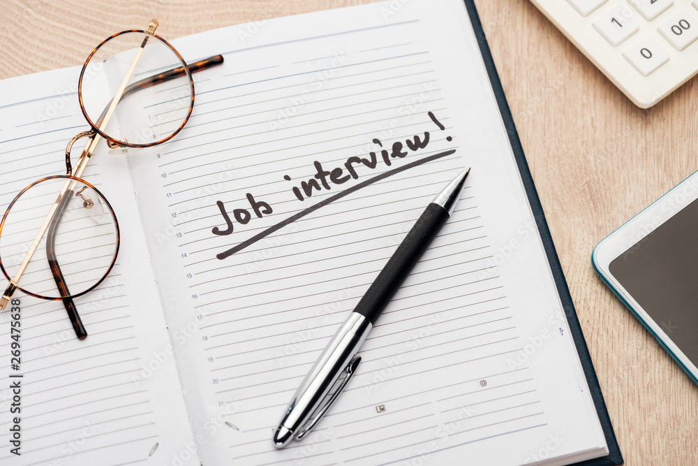 notebook with pen, glasses and job interview lettering on wooden table notebook with pen, glasses and job interview lettering on wooden table