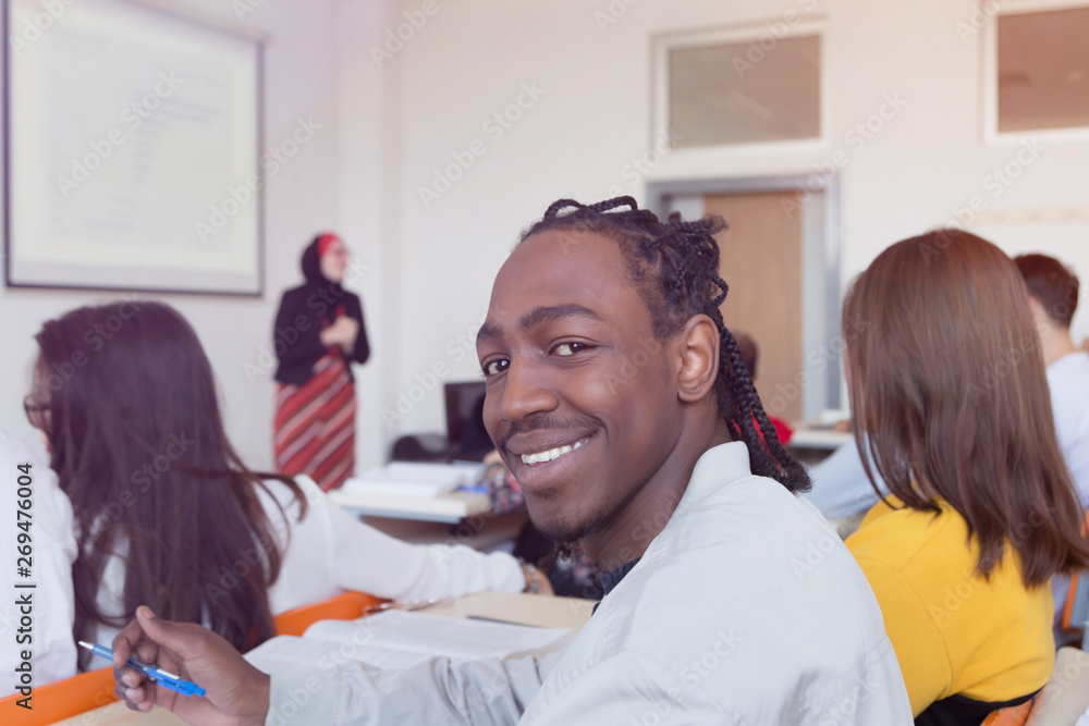 African american male student smiling into camera during class. Female muslim professor explain lesson to students and interact with them in the classroom.Helping a students during class. African american male student smiling into camera during class. Female muslim professor explain lesson to students and interact with them in the classroom.Helping a students during class.
