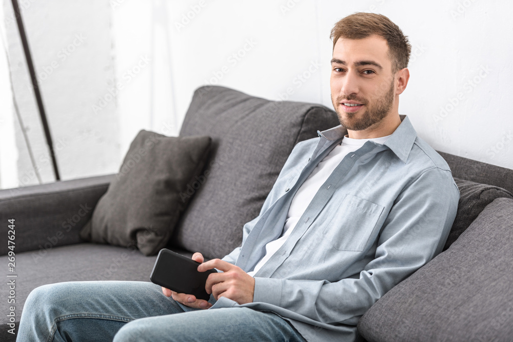 bearded man sitting on sofa and holding smartphone in living room bearded man sitting on sofa and holding smartphone in living room
