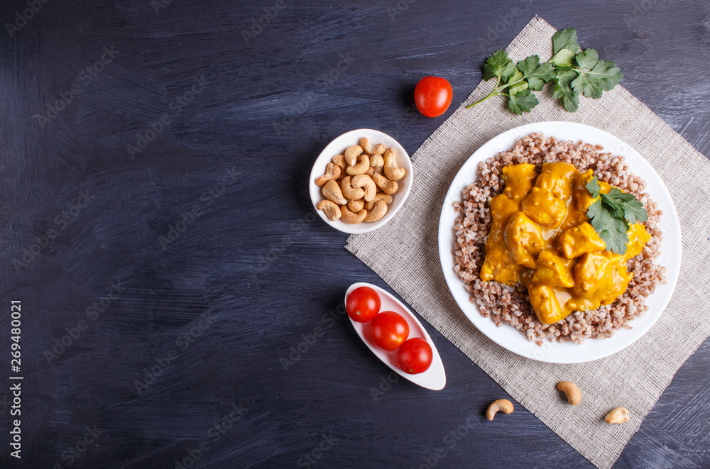 Buckwheat with chicken curry sauce with cashew on black wooden background.