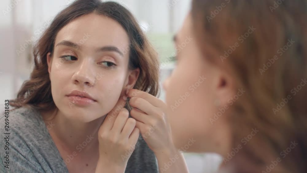 Cheerful woman putting earrings to ear looking in bathroom mirror at home Cheerful woman putting earrings to ear looking in bathroom mirror at home