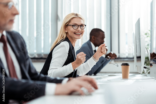 selective focus of cheerful businesswoman smiling near men in office