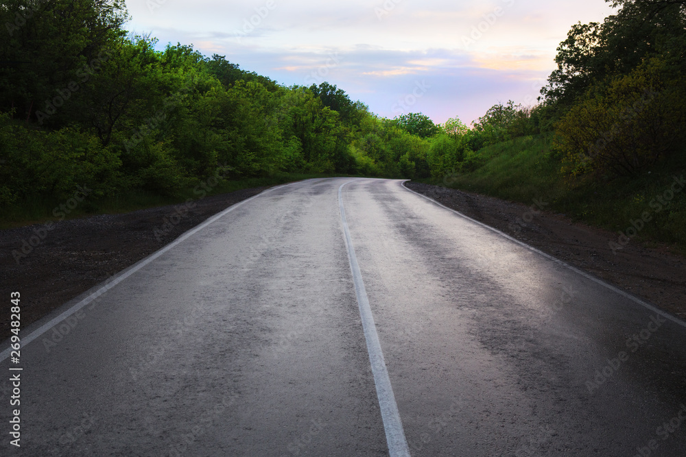 Obraz premium Asphalt highway in the forest in the evening at sunset
