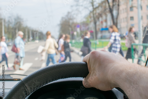 view from the car, the man's hand on the steering wheel of the car, located opposite the pedestrian crossing and pedestrians crossing the road