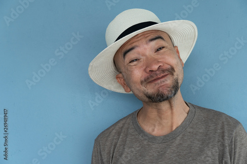portrait of 30-40s Japanese adult man funny grinding with summer hat on blue gray wall background