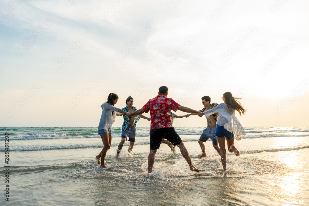 A group of male and female friends who play fun on the sea beach amid the sunset. - obrazy, fototapety, plakaty 