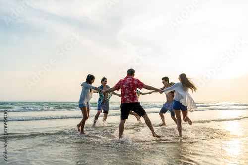 A group of male and female friends who play fun on the sea beach amid the sunset.