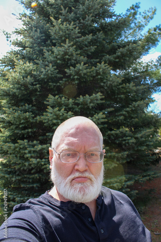 Portrait of senior man in front of blue spruce tree
