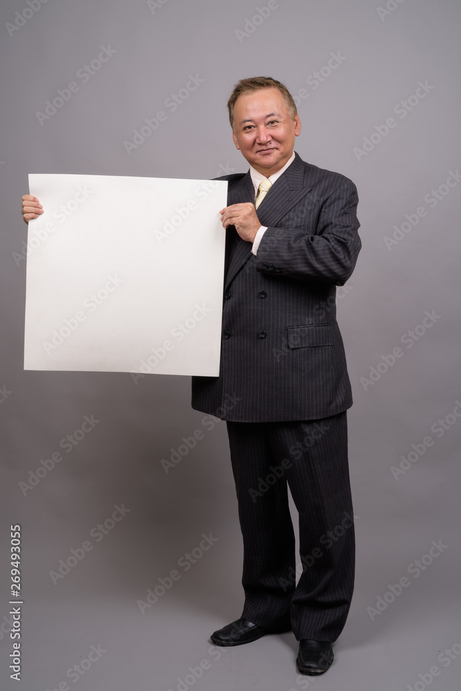 Portrait of mature Asian businessman against gray background Portrait of mature Asian businessman against gray background