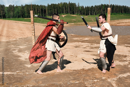 A concept photo of a Roman battle of two warriors of the Colosseum in action with aggressive emotions in full military uniform on a desert landscape on a sunny day with a dry sun.