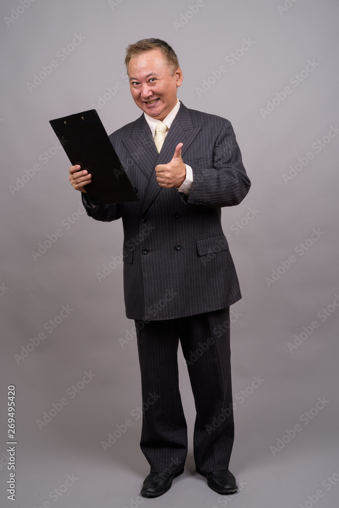 Portrait of mature Asian businessman against gray background Portrait of mature Asian businessman against gray background