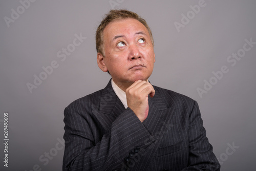 Portrait of mature Asian businessman against gray background © Ranta Images