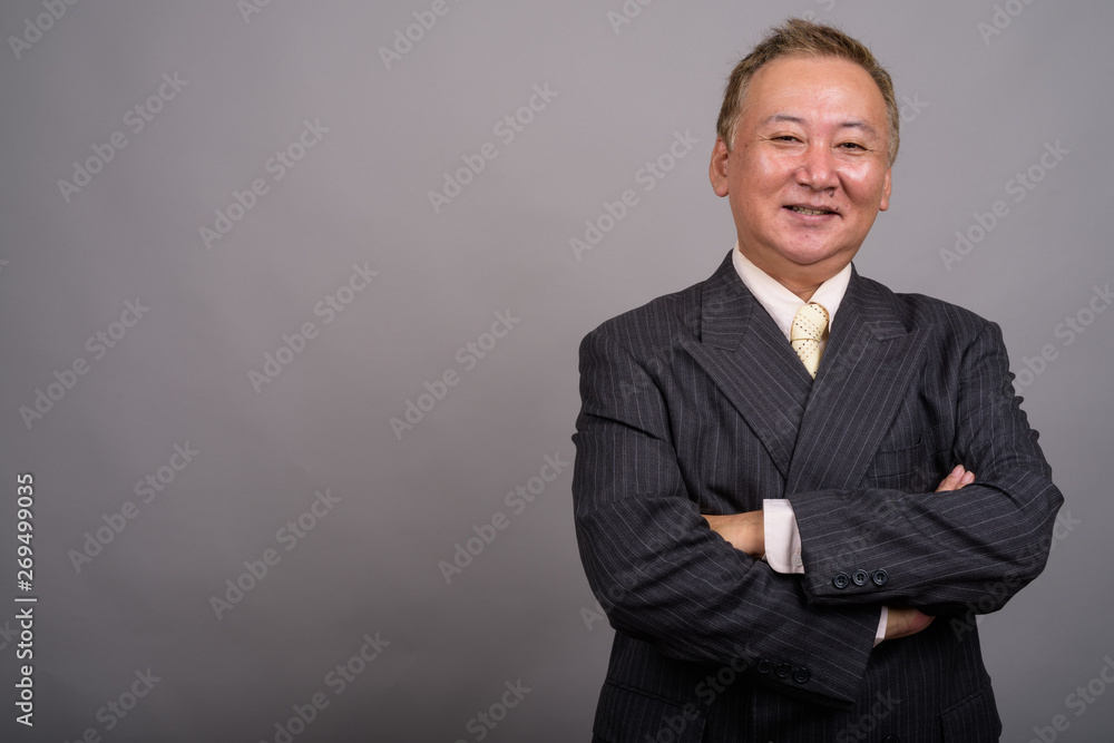 Portrait of mature Asian businessman against gray background - obrazy, fototapety, plakaty 