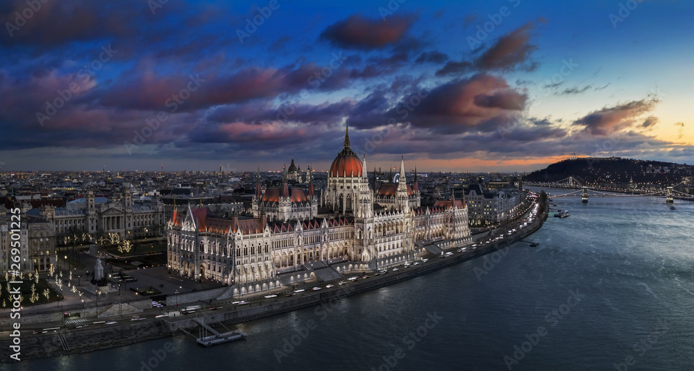 Obraz premium Budapest, Hungary - Aerial panoramic view of the beautiful illuminated Parliament of Hungary with Szechenyi Chain Bridge, Statue of Liberty and colurful clouds at background at sunset