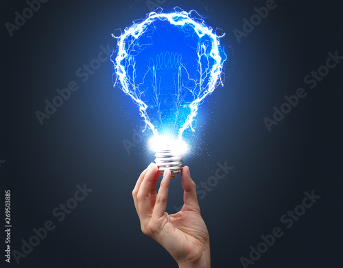 Hand holding shiny light bulb on dark background. New idea concept