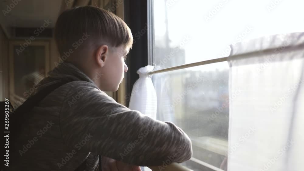 The boy stands at the train window and looks out the window at the running landscapes. Travel by train. Tourism on vacation, travel around the world. The boy stands at the train window and looks out the window at the running landscapes. Travel by train. Tourism on vacation, travel around the world.