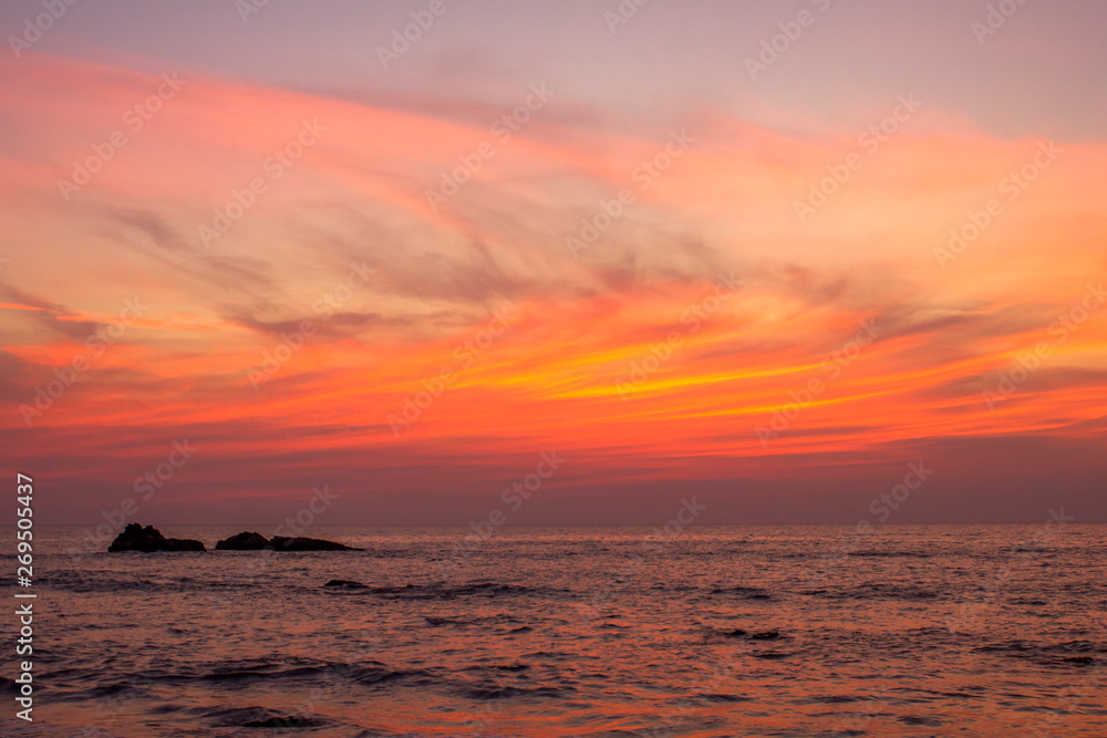 ocean under bright orange clouds in a purple sunset sky