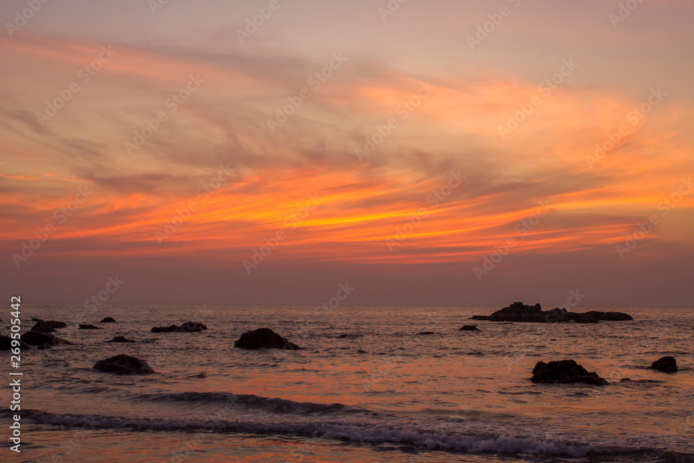 dark silhouettes of stones in the sea against the background of bright orange clouds in a purple sunset sky