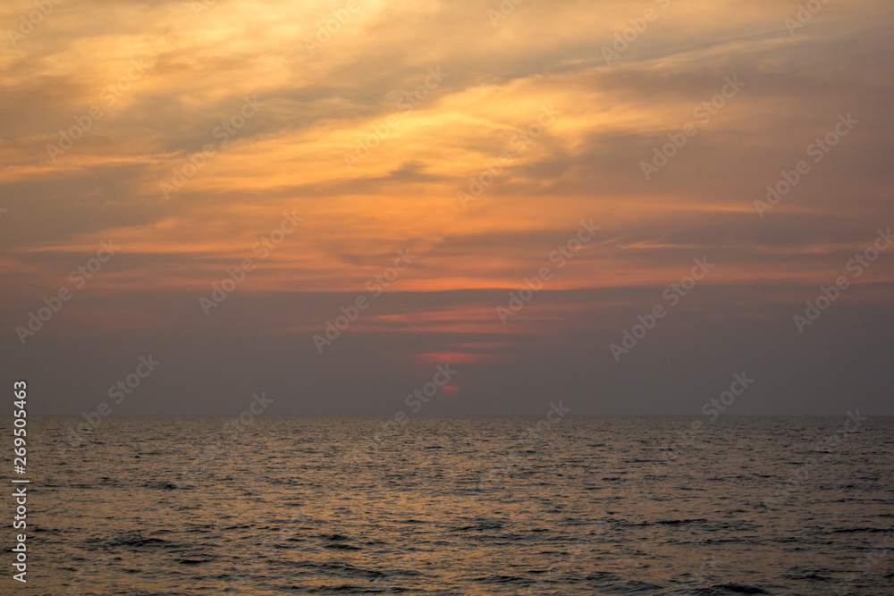 ocean under a purple sunset sky with bright yellow clouds