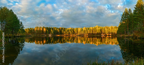 The forest lake at sunset, with reflection of sky and forest on a water smooth surface, a panorama from several frames, Russia, Mari El