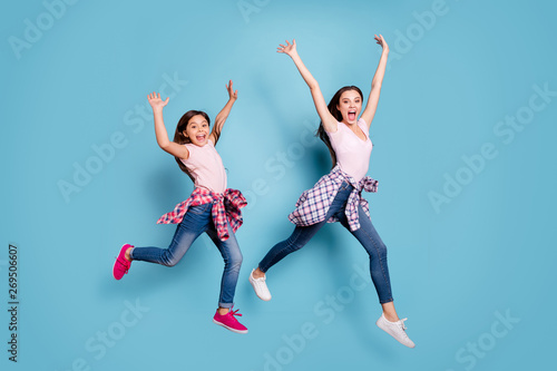Full length body size view portrait of two nice attractive cheerful cheery straight-haired girls hipster outfit raising hands having fun isolated on bright vivid shine blue turquoise background