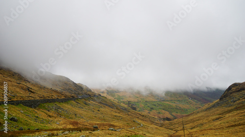 Stunning landscape with foggy and moody skies among the mountains, covered with saturated grass – captured during a hike at Snowdon in winter (Wales, United Kingdom)