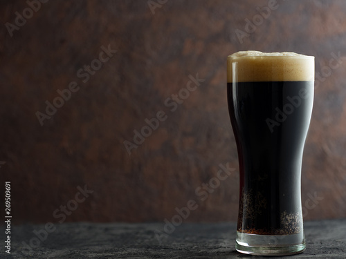 Craft dark beer porter in a glass on a brown dark background with copyspace