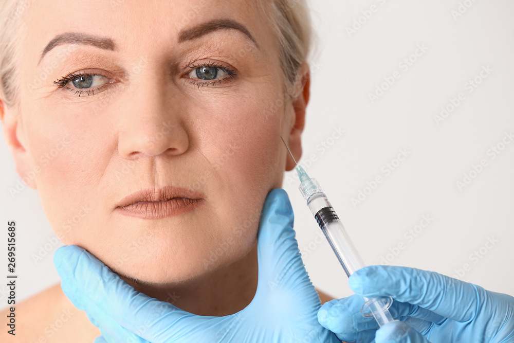 Mature woman receiving injection in face on light background, closeup Mature woman receiving injection in face on light background, closeup