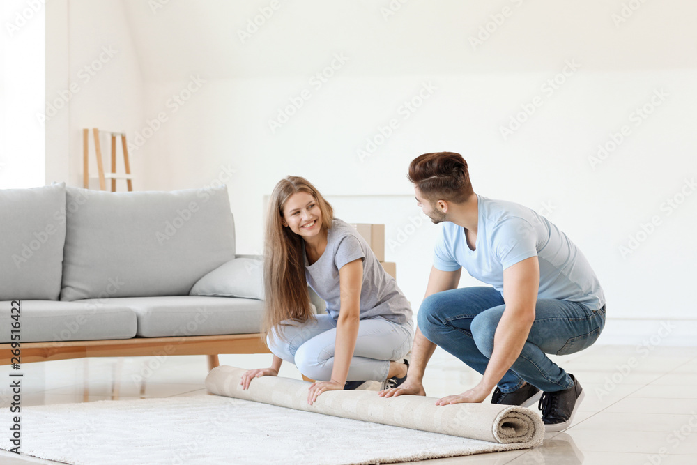 Young couple unrolling carpet on floor Young couple unrolling carpet on floor