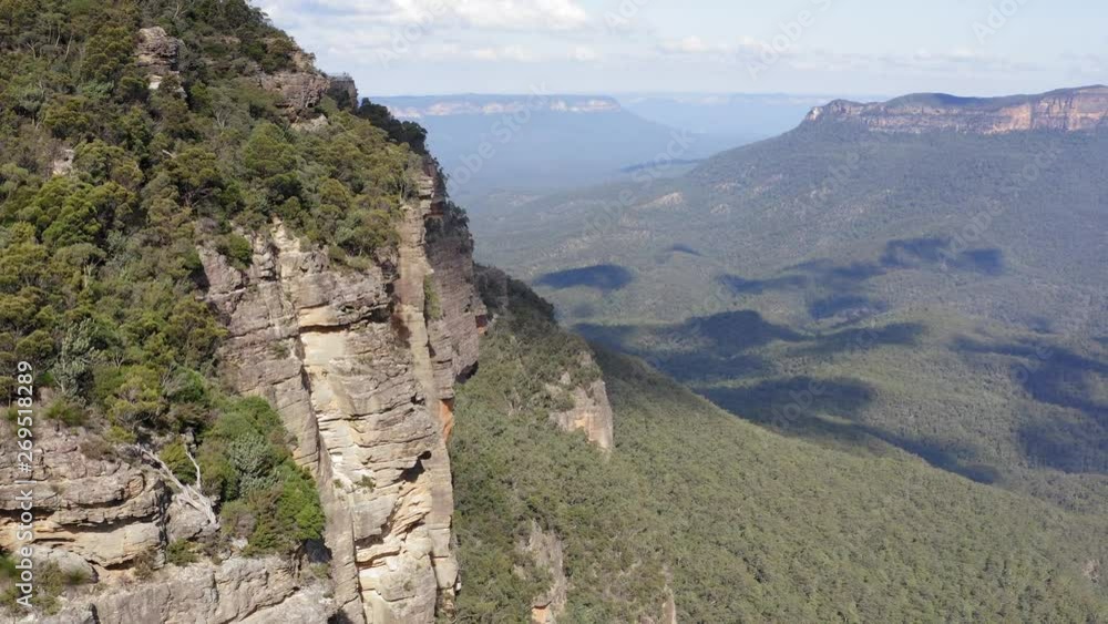 Flying close along a cliff line in the mountains towards people standing at a lookout Flying close along a cliff line in the mountains towards people standing at a lookout