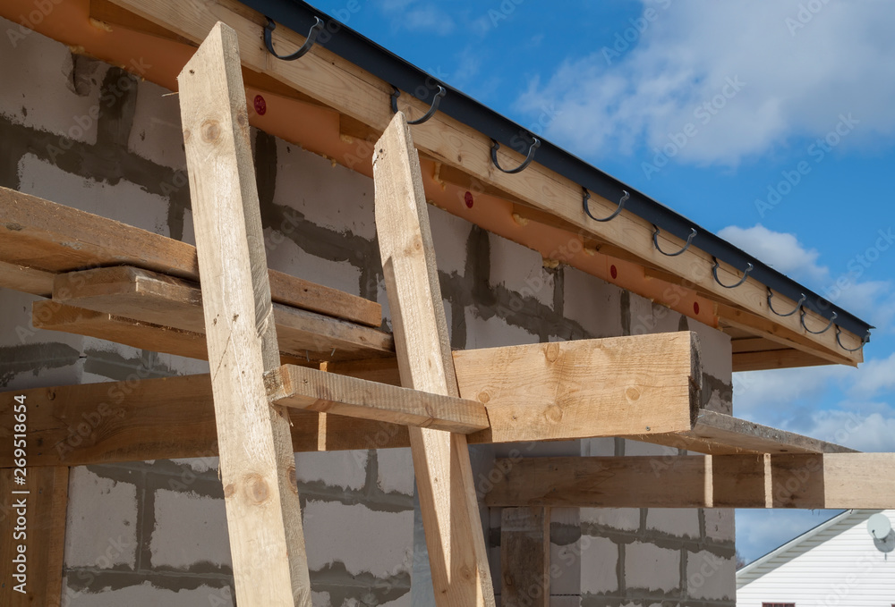 close up view of scaffolding and house under construction with holders for gutters water drainage system of roof close up view of scaffolding and house under construction with holders for gutters water drainage system of roof