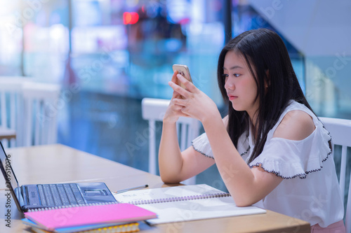 Portrait of young asian female student using her mobile phone sending a text outside at cafe.