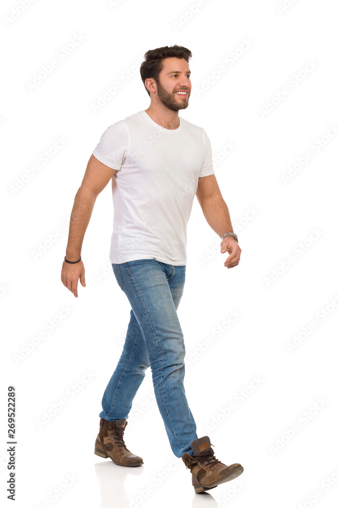 Handsome Man In White T-shirt, Jeans And Boots Is Walking And Smiling Handsome Man In White T-shirt, Jeans And Boots Is Walking And Smiling