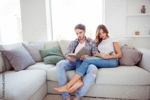 Portrait of his he her she nice attractive lovely charming focused concentrated couple spending day sitting on cosy divan in light white style interior living room house indoors