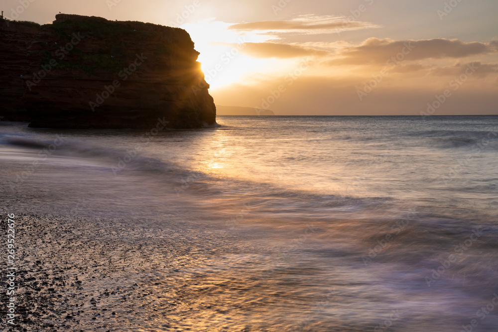 Stunning sunrise landscape image of Ladram Bay beach in Devon England with beautiful rock stacks on beach