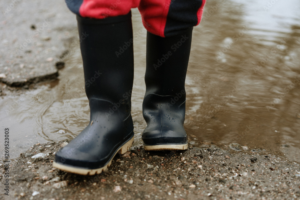 child walks after rain through the puddles in rubber boots child walks after rain through the puddles in rubber boots