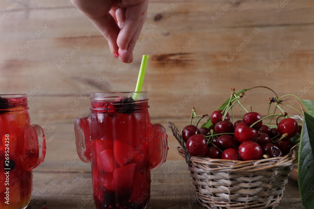 Compote from fresh sweet cherry in a glass with fresh sweet cherry in a wicker basket on a wooden background Compote from fresh sweet cherry in a glass with fresh sweet cherry in a wicker basket on a wooden background